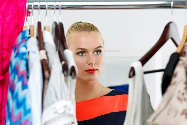 Beautiful thoughtful blonde woman standing inside wardrobe rack