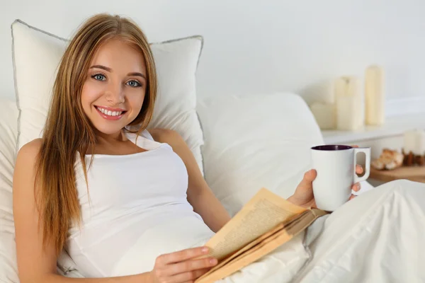 Young beautiful smiling blonde woman lying in bed reading old bo