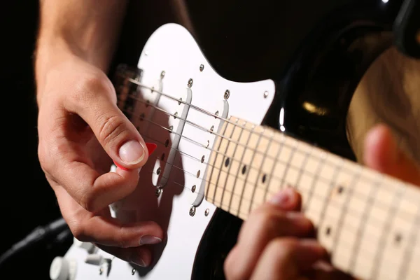Male hands playing electric guitar with plectrum closeup