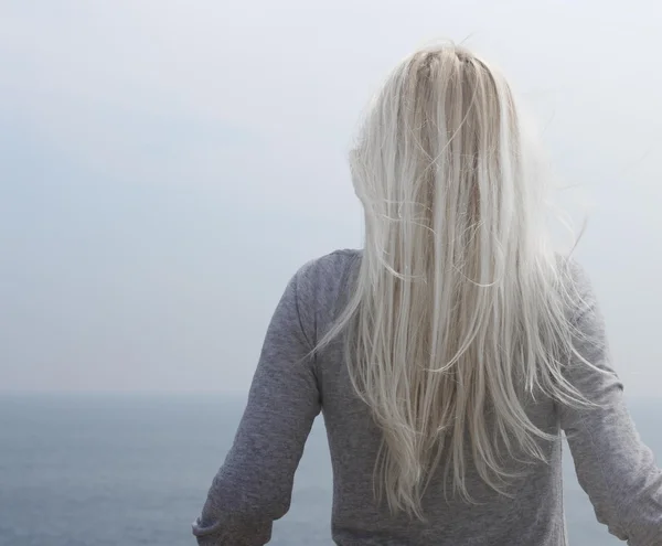 Blond girl standing against the sea from her back