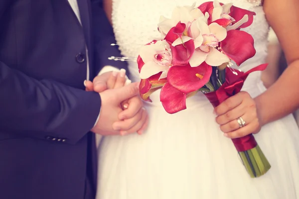 Hands of a bride and groom. Bride holding red lily bouquet