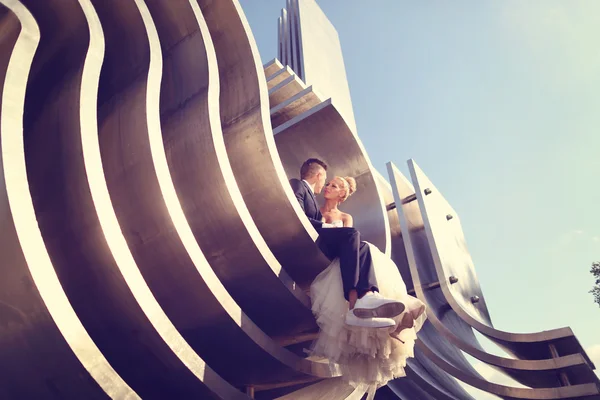 Bride and groom sitting on architectural metallic piece