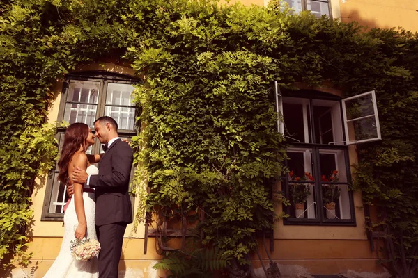 Bride and groom embracing in front of a beautiful house covered with ivy