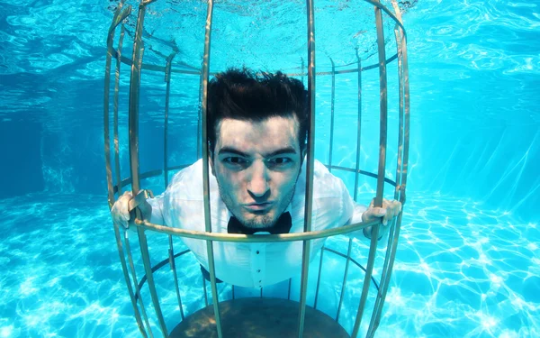 Funny groom underwater in a bird cage