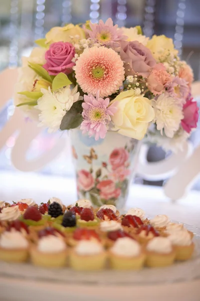 Beautiful bouquet in vase with colorful flowers and sweets on table