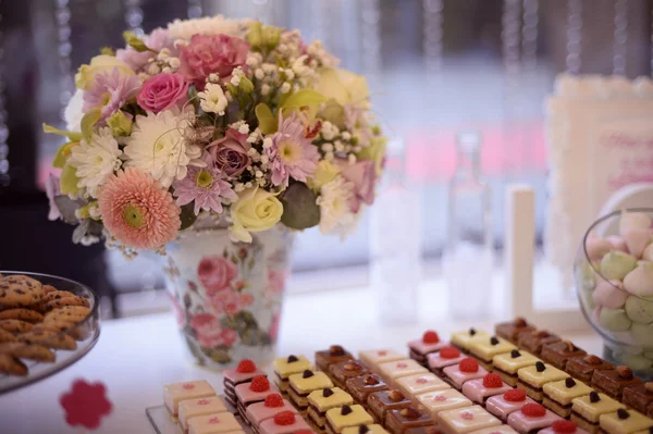 Beautiful bouquet in vase with colorful flowers and sweets on table