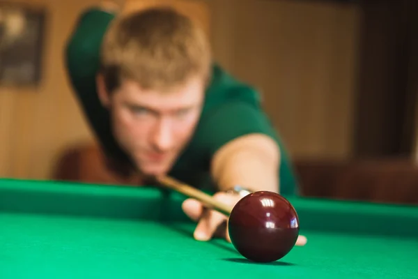 Details of the game of billiards. Red ball in the center of the frame. Player aiming cue in a billiard ball. Blurred person in the background.