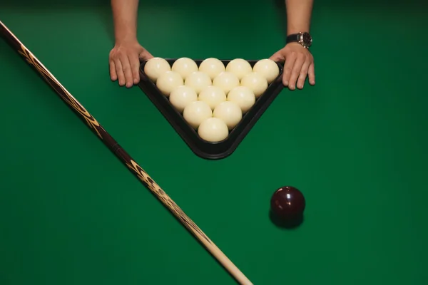 The order on the table. Balls neatly folded into a triangle. Details of the game of billiards. In the picture, there are men's hands. Billiard game concept.