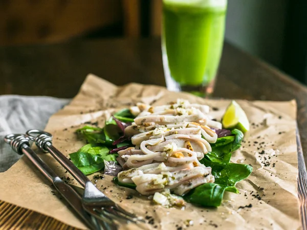 Fried squid with lemon and greens and lime wedge on a board, green juice on the background