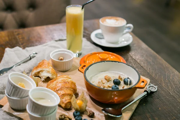Breakfast with porridge and croissant decorated with blueberries and nuts, glass of orange juice and cappuccino