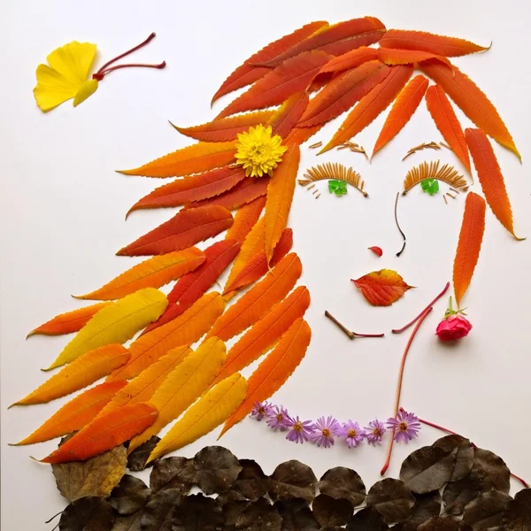 Art composition: female face made of red autumn leaves and flowers
