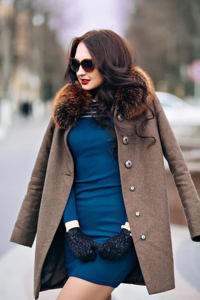 Fashion Outdoors Sexy glamor young woman with chic long dark hair beautiful young brunette girl wearing stylish sunglasses, trendy green dress, luxurious fur coats and gloves, fashion makeup posing in
