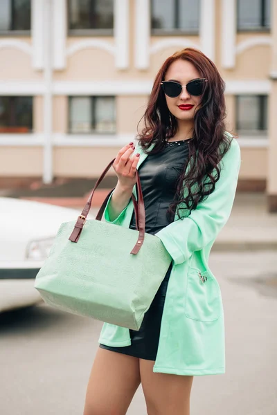 Funny model in sunglasses and in a little green dress, white background. Fashion lifestyle portrait of young happy pretty woman laughing and having fun on the party. favorite music at earphones