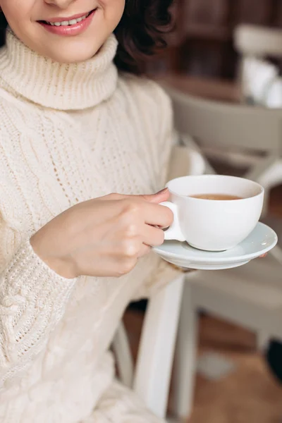 Female model with long hair. Amazing sensual girl with gorgeous make-up is enjoying a delicious coffee or tea, playfully smiling at the camera. Long dark wavy hair, white smile.