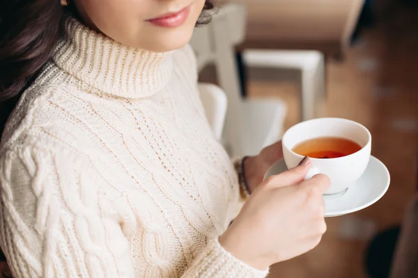 Coffee. Beautiful Girl Drinking Tea or Coffee. Cup of Hot Beverage. Brunette in a cafe drinking tea, eating sweets, reading a book, beautiful eyes and gorgeous makeup, wavy hair.