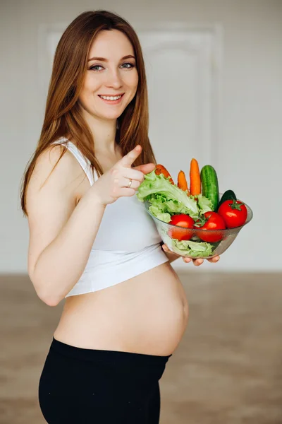 Healthy nutrition and pregnancy. Close-up pregnant womans belly and vegetable salad. A beautiful pregnancy woman eating healthy food