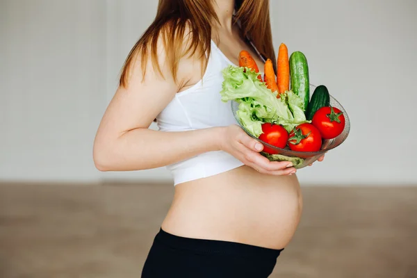 Healthy nutrition and pregnancy. Close-up pregnant womans belly and vegetable salad. A beautiful pregnancy woman eating healthy food