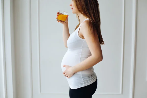 Pregnant woman drinking orange juice bottle after training.  Young pregnant woman with glass with juice isolated on white background. Nutrition and diet during pregnancy.