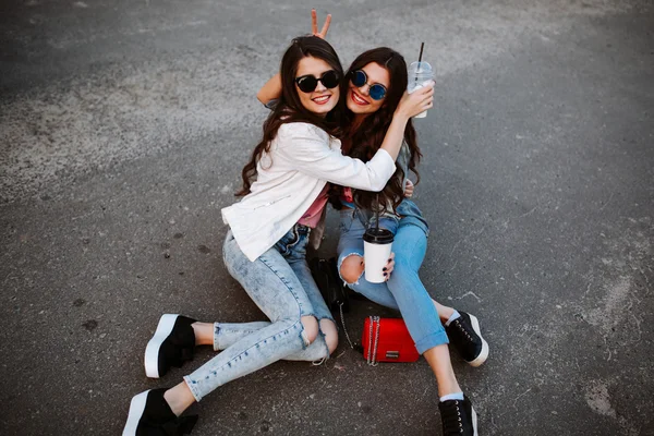 Summer lifestyle portrait of two hipster stylish women with fit sexy body, wearing denim outfit and vintage sunglasses. Girls friends going crazy, having fun, dancing, laughing and screaming.