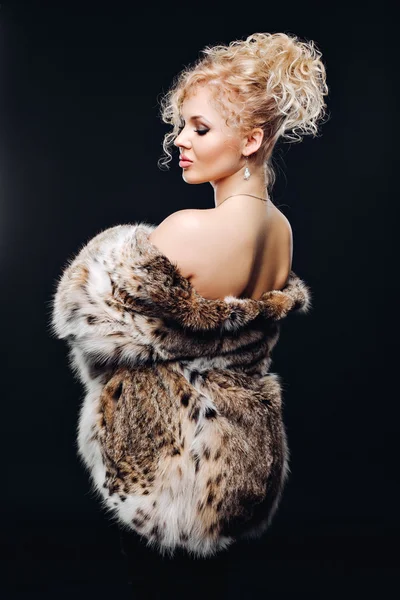 Amazing woman in lynx fur coat in mirrored sun glasses, a chic fur coat. Portrait of a woman in Studio on a black background in furs,luxury makeup, luxury bust. Advertise a fur coat from a lynx.