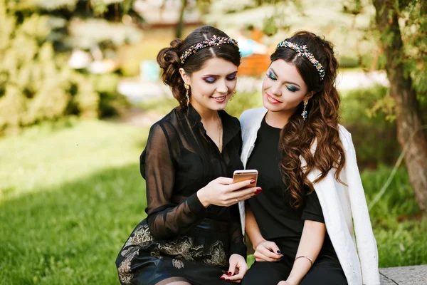 Friend look at the phone and discuss something. Laughing and smiling, going crazy, having fun. Young stylish woman at the party with a bright evening make-up and fashionable jewelry.