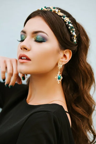 Portrait of fashionable girl brunette with a gorgeous bright makeup. The eyes are closed. Stylish expensive jewelry, a headband, a Hoop with precious stones, diamond earrings.