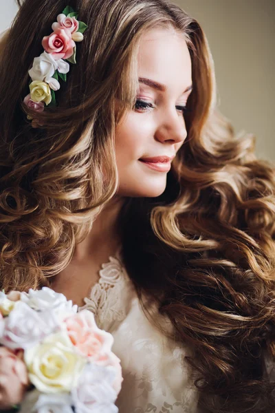 Beautiful young bride with long curly hair in white lingerie and robe sitting on a chair in the room and waiting for the groom. Morning of the bride