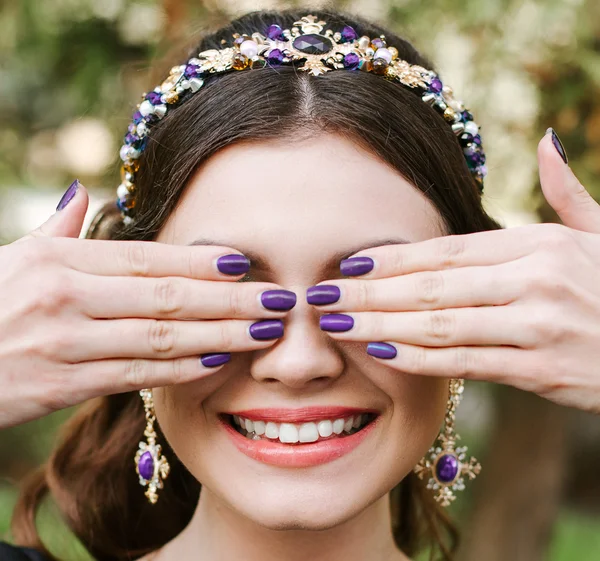 Fashion, beauty, tenderness. Young happy woman with a bright manicure smile wide,white smile,straight white teeth. The girl covers her face with hands. Hair band, earrings, lilac purple nail Polish.