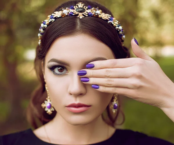 Close-up portrait of beautiful fashion woman with bright purple manicure, stylish makeup. The girl is holding a hand near the face, covering one eye. Manicure, design, fashion, make-up, brightly. The