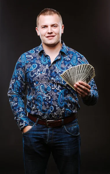 Portrait of a man in a shirt and jeans holds a lot of hundred dollar bills. The guy is holding a salary, money.