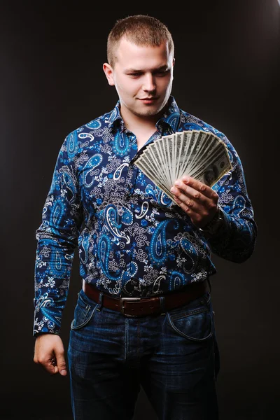 Portrait of a man in a shirt and jeans holds a lot of hundred dollar bills. The guy is holding a salary, money.
