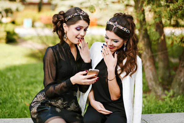 Friend look at the phone and discuss something. Laughing and smiling, going crazy, having fun. Young stylish woman at the party with a bright evening make-up and fashionable jewelry.