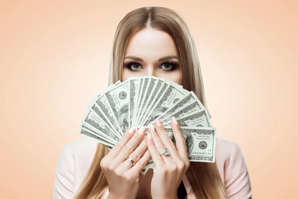 Woman with a fan of money in her hands. Beauty portrait of young girl covers her face with money. Bills of 100 USD. Studio light background. Isolated on brown background. Makeup bright gold.