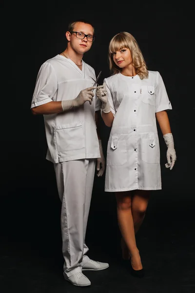 Portrait two doctors wearing white medical uniform holding a pair of scissors and tweezers in both hands