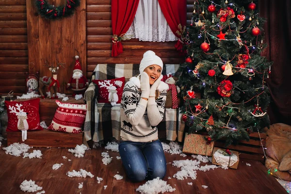 Beautiful girl in sweater gloves hats New Year with gifts around the Christmas tree and fireplace