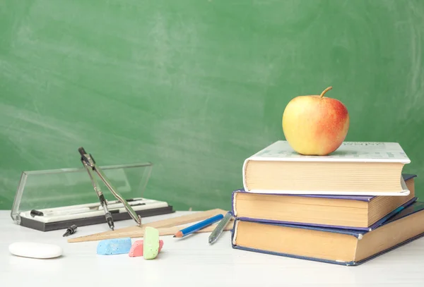 Books and supplies for school on the table next to chalk Board