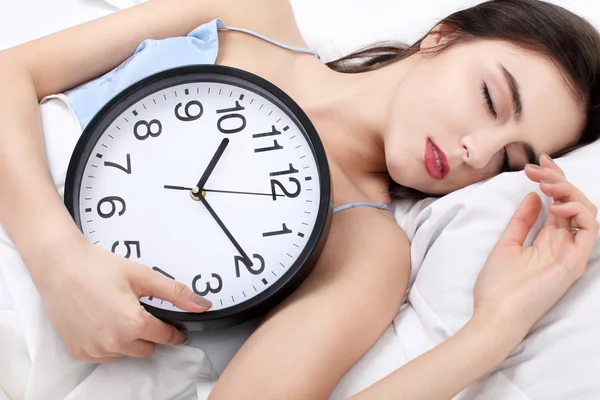 Beautiful sleeping woman resting in bed with alarm clock ready to wake her in the morning.