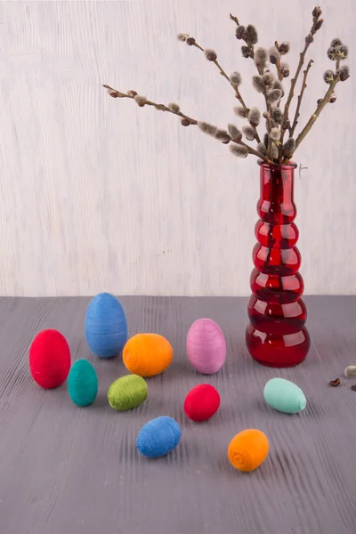 Willow branches in a red twisted vase with multi-colored knitted eggs on a gray background
