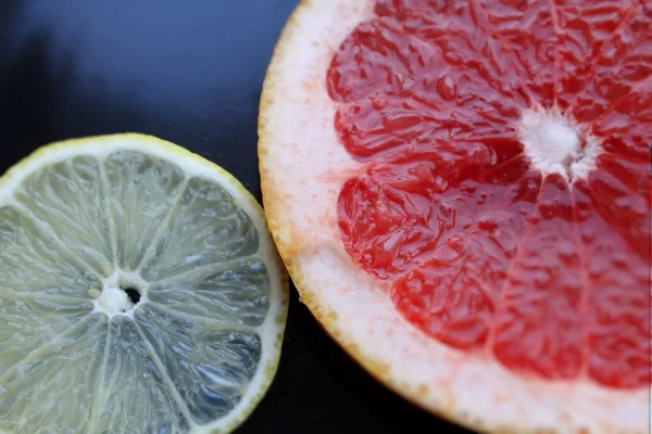 Sliced grapefruit and lemon on black glossy background