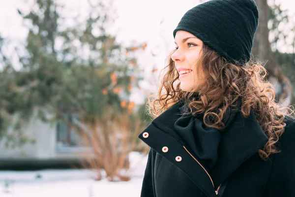 Happy smiling girl with curly hair in a coat and hat in winter p