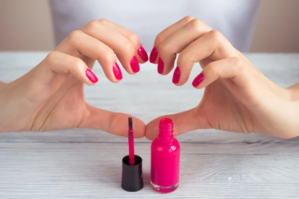 Female hands with pink manicure and the open bottle of varnish o