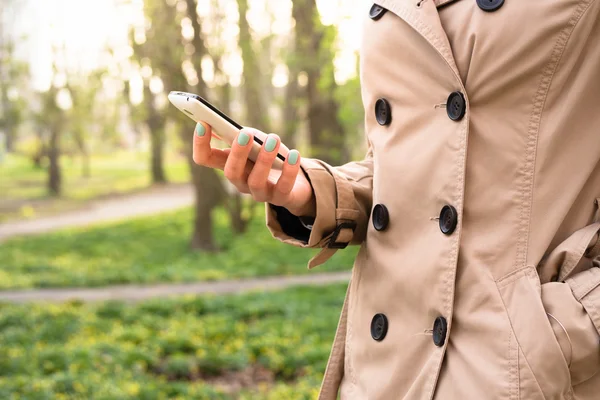 Woman in beige coat walks in the park and using a mobile phone