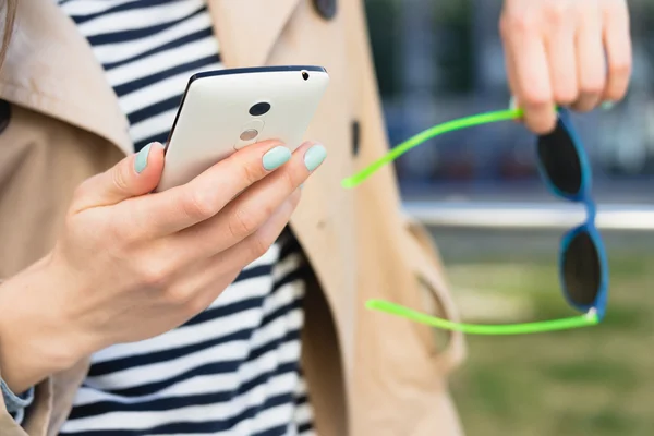 Girl in a beige jacket and a striped shirt holding mobile phone