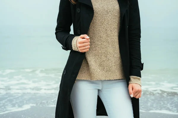 Slim woman in jeans, a sweater and a black coat against the sea
