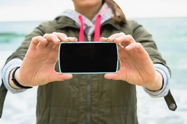 Girl in the green jacket shows a blank phone screen on a backgro