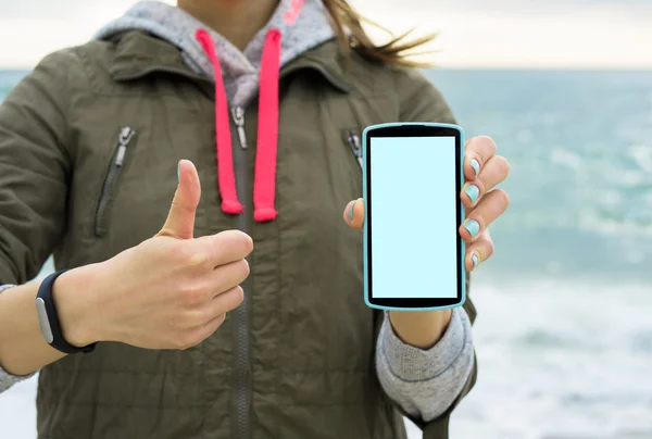 Girl in the green jacket on the beach showing the mobile phone s