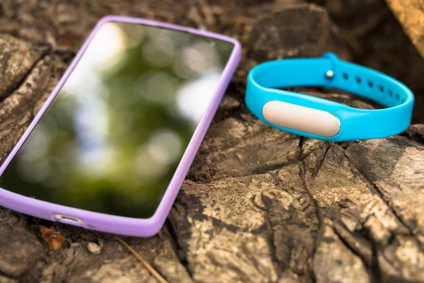 Fitness tracker and smart phone lying on a tree stump in the for
