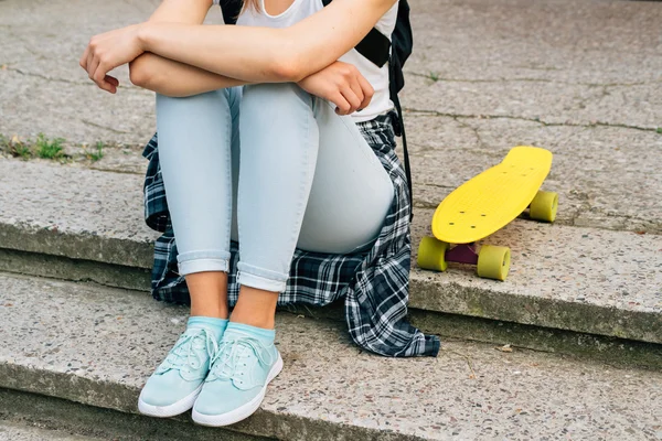 Girl in jeans, sneakers and t-shirt sitting on the steps next to