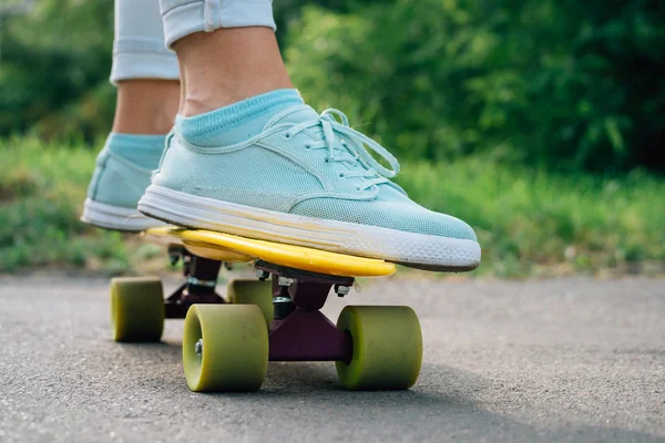 Female feet in sneakers on a yellow skateboard closeup