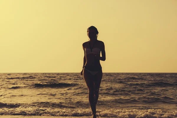 Woman in a swimsuit runs out of the water on the beach